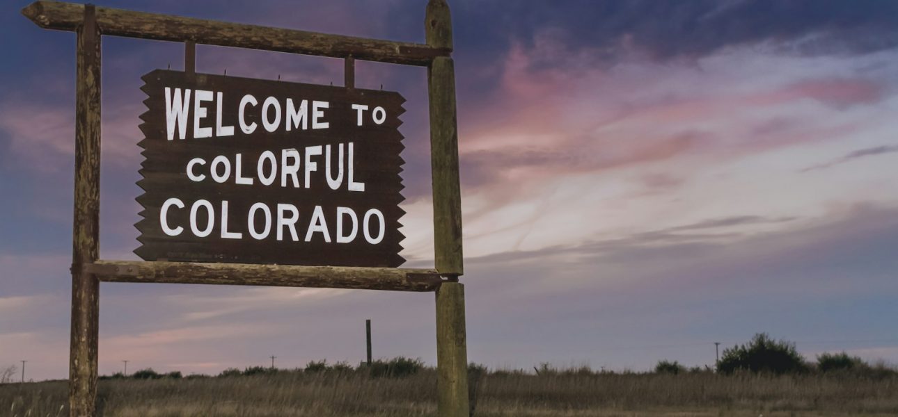 welcome to colorful Colorado sign near green field under blue and orange skies during daytime