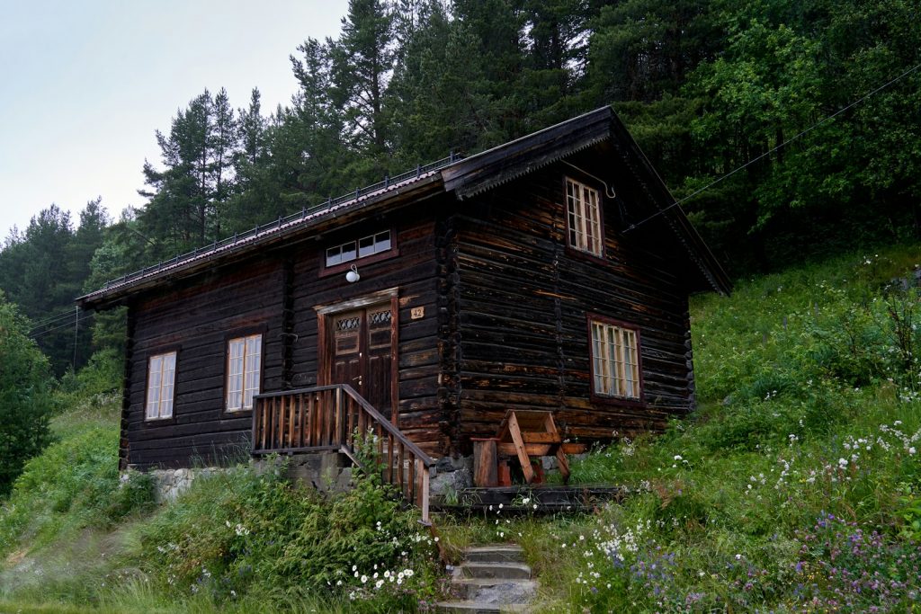 A wooden cabin sits on a grassy hillside.