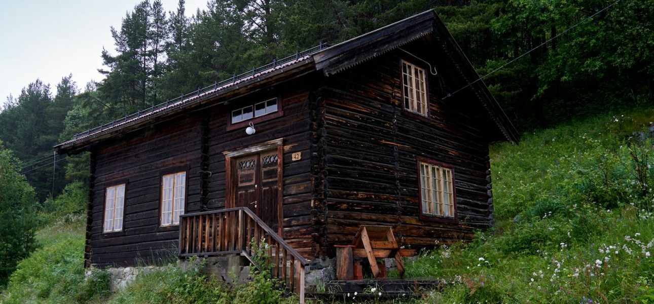 A wooden cabin sits on a grassy hillside.