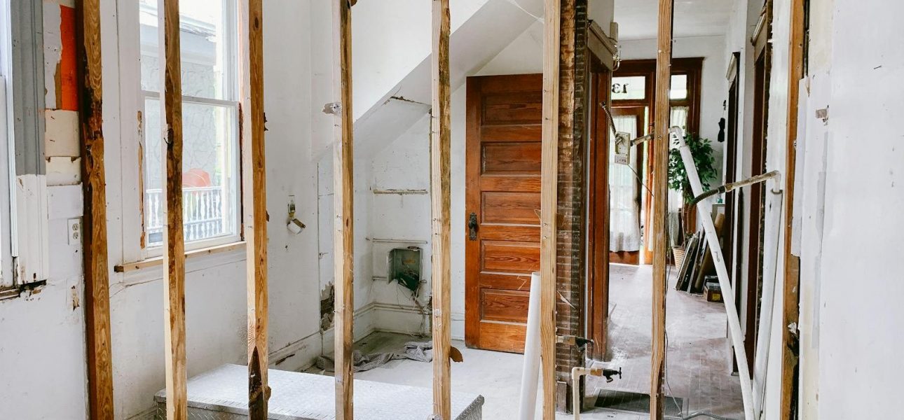 Interior view of a home under renovation with exposed wooden beams and door.