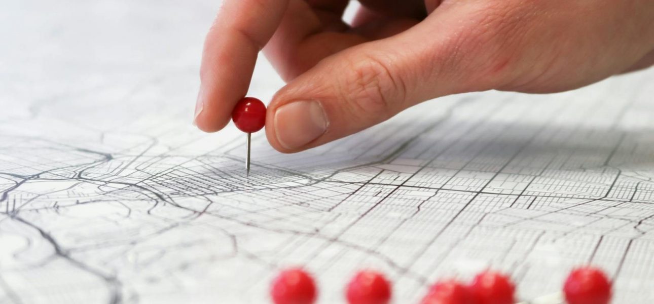 Close-up of a hand placing a red pin on a map indicating geographic location pinning.