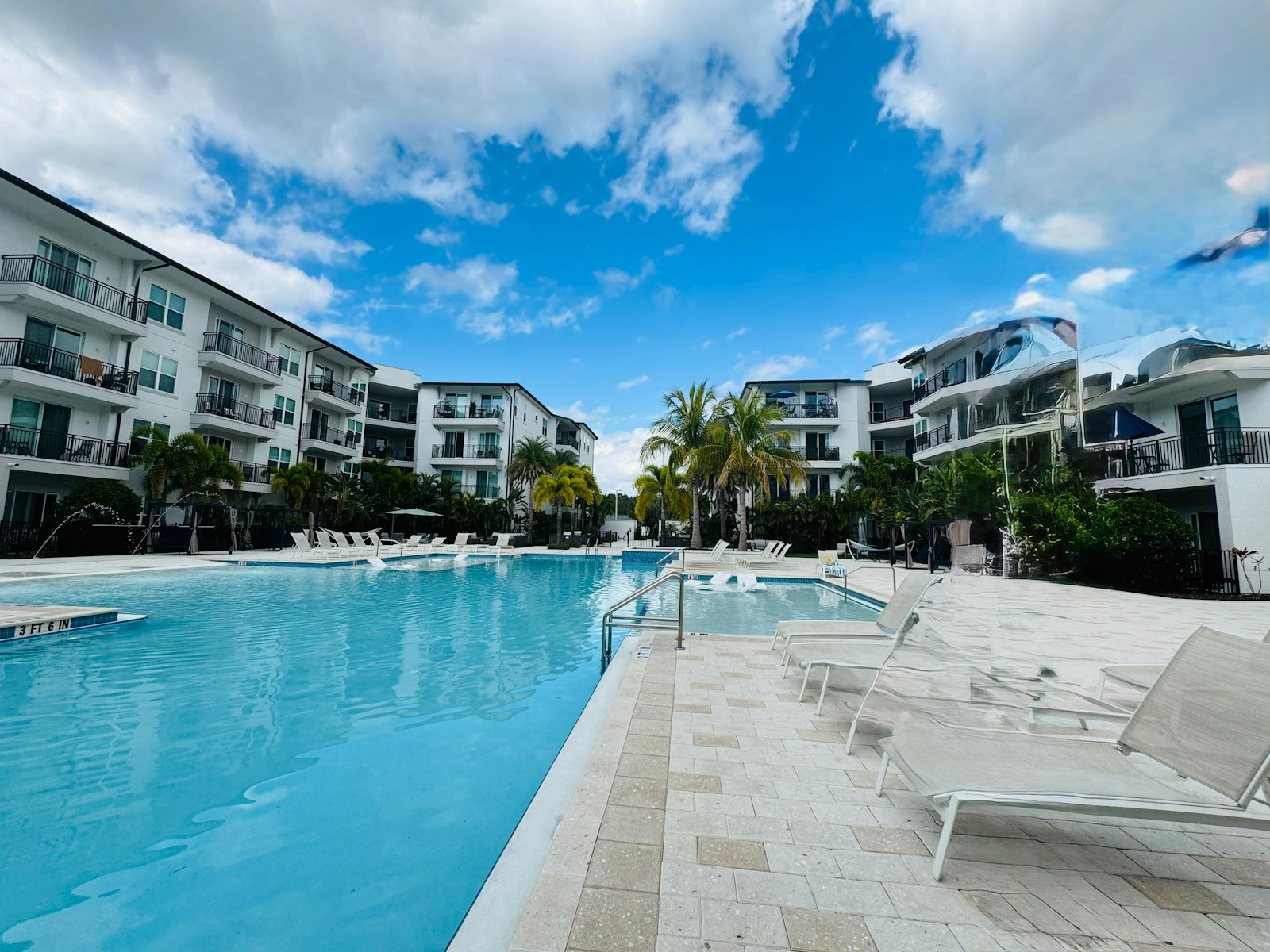 Swimming pool and lounge deck at a garden-style apartment community under a blue sky