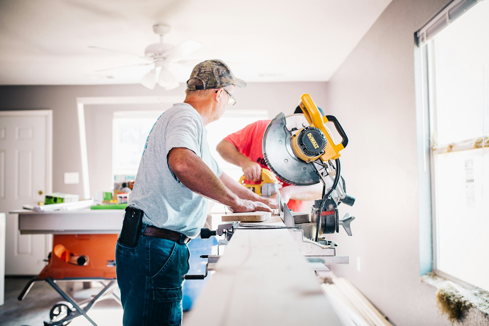 Two contractors working a miter saw inside a house under renovation